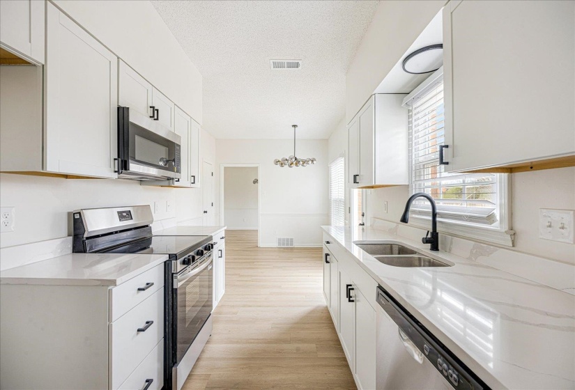 Modern kitchen featuring white cabinetry, quartz-finish countertops, stainless steel appliances, a double basin sink with a matte black faucet, and wood-finish flooring