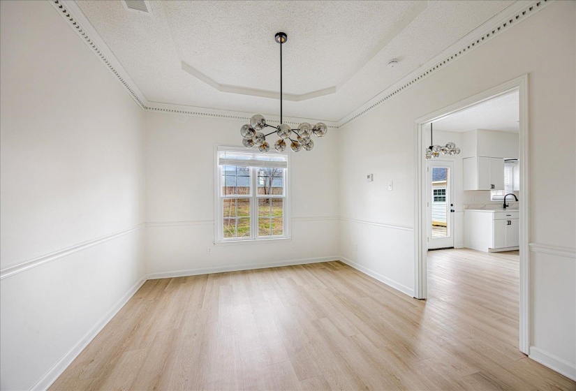 Spacious room featuring light wood-finish flooring, white walls with wainscoting and crown molding, and a contemporary chandelier