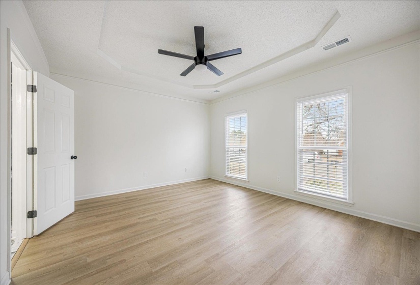 Spacious room featuring light wood-finish flooring, a tray ceiling, and a modern black ceiling fan