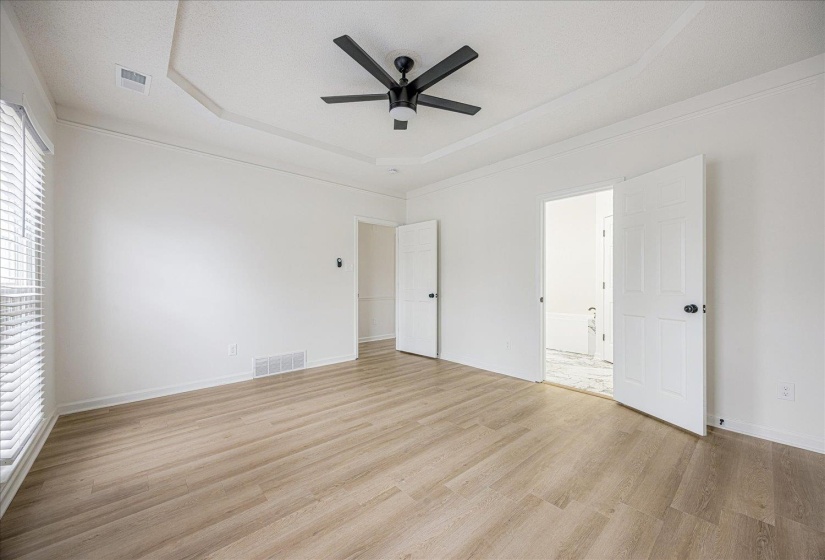 Spacious room featuring wood-finish flooring, a tray ceiling, and a modern ceiling fan with lighting
