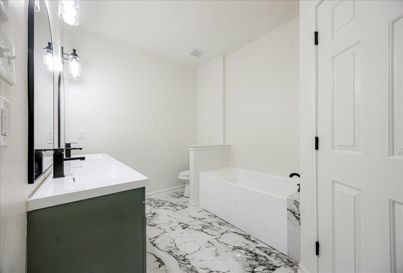 Contemporary bathroom featuring a dark green dual vanity with white countertops, a deep soaking tub, and black-accented fixtures