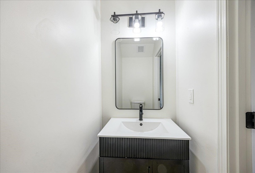 Bathroom vanity featuring a white countertop with an integrated sink, matte black faucet, and a black vanity cabinet with textured paneling