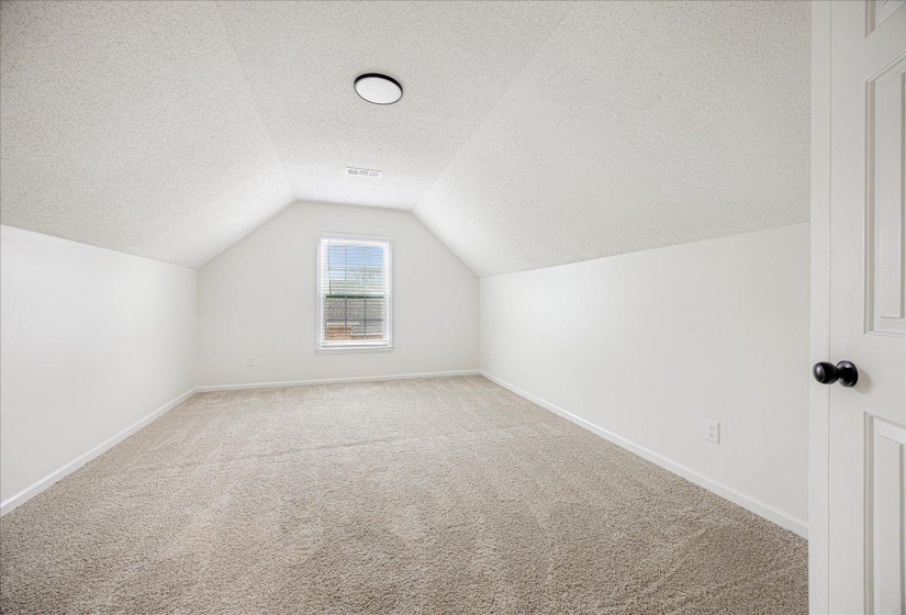 Attic room with sloped ceilings and light-toned carpeting