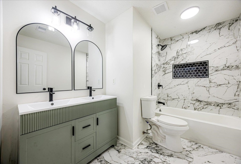 Bathroom featuring a green dual vanity with integrated sinks, black hardware, and two arched mirrors