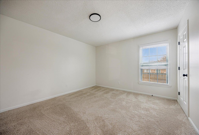 Carpeted room with white walls, a single window featuring horizontal blinds, and a white paneled door with black hardware