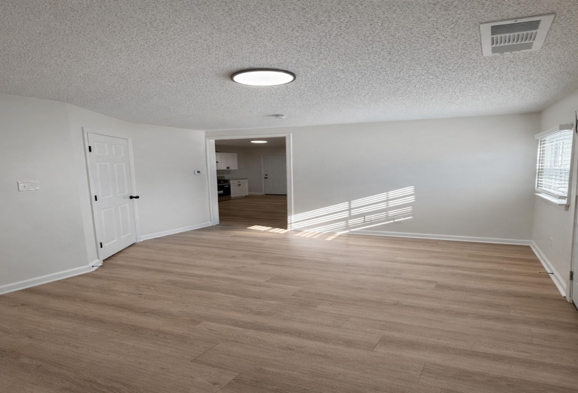 Open-concept living space with wood-finish flooring, white walls, and a contemporary ceiling light fixture