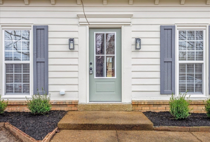 Entryway featuring a light green paneled door with glass inserts, flanked by two windows with white grilles and dark gray louvered shutters