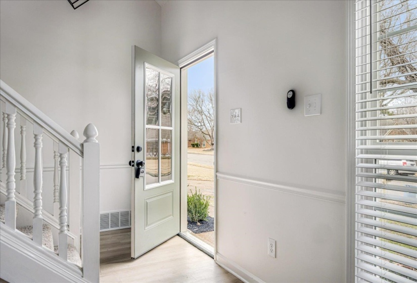 Entryway featuring a decorative glass paneled door, wood-finish flooring, white painted walls with wainscoting, and a white staircase with balusters