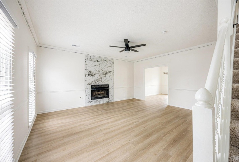 Spacious room featuring wood-finish flooring, a white-tiled fireplace, wainscoting, crown molding, and a ceiling fan