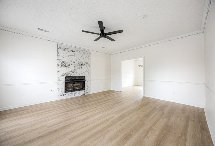 Spacious living area featuring a marble-style fireplace surround, wood-finish flooring, a modern black ceiling fan, white wainscoting, and decorative crown molding