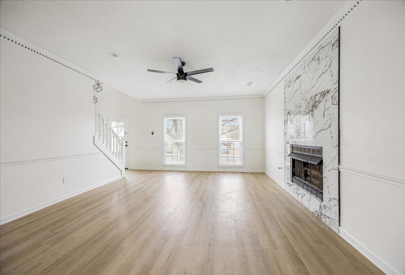 Spacious interior featuring wood-finish flooring, a contemporary ceiling fan, and a fireplace with a striking floor-to-ceiling marbled surround
