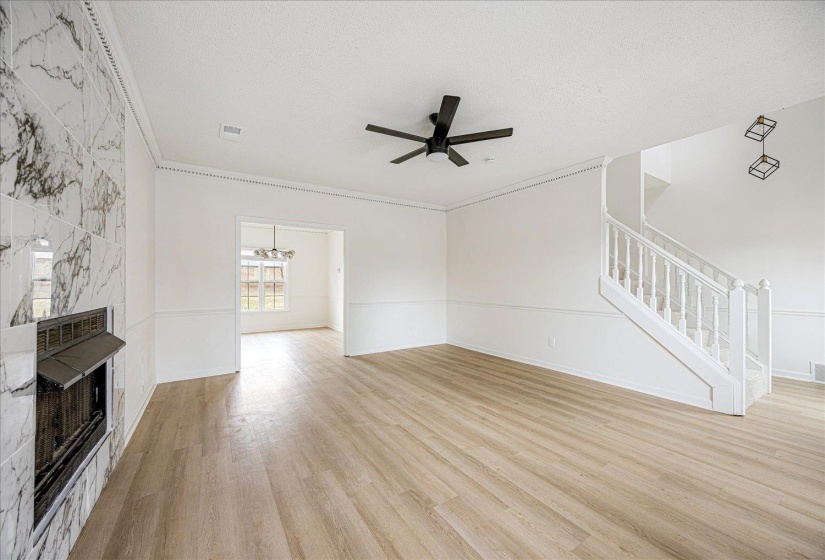 Spacious living area featuring wood-finish flooring, a white marble-look tile fireplace, and a contemporary ceiling fan