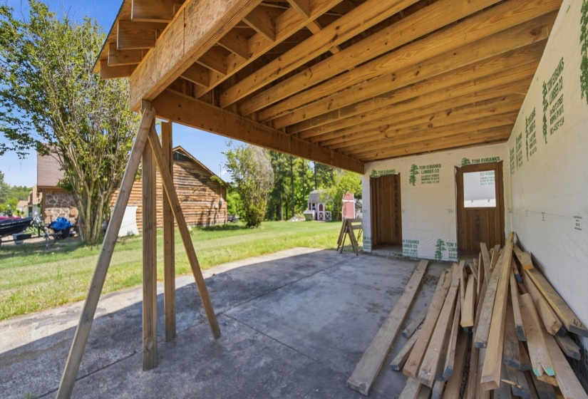 Open-air garage space with exposed wood joist ceiling, concrete flooring, and two framed entryways
