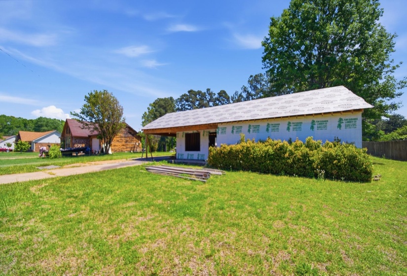 Single-story structure under construction featuring exterior sheathing, a partially finished roofline, and an attached covered area