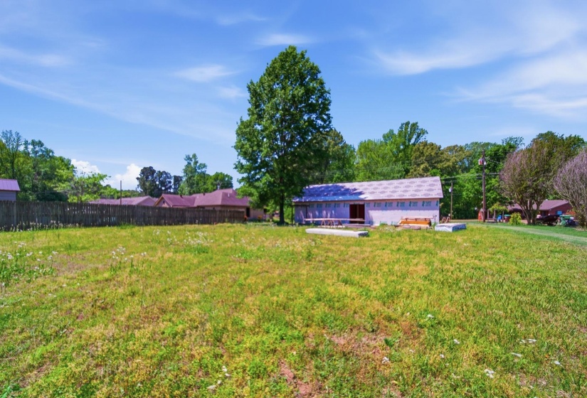 Expansive grassy lot featuring a partially constructed structure with a light-colored exterior and a visible roofline