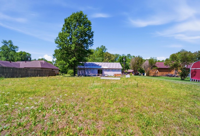 Expansive open field featuring distant structures and mature trees under a clear sky