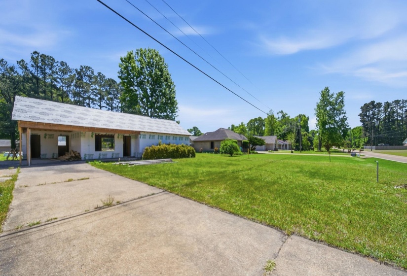 Building under construction featuring a newly installed roof, multiple framed window openings, and a concrete driveway