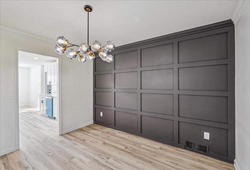 Dining area featuring a contemporary multi-bulb chandelier, a full wall of dark paneling, crown molding, and wood-finish flooring