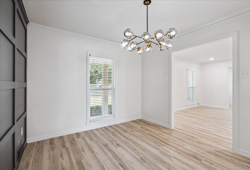 Spacious room featuring wood-finish flooring, a modern multi-bulb chandelier, and crown molding