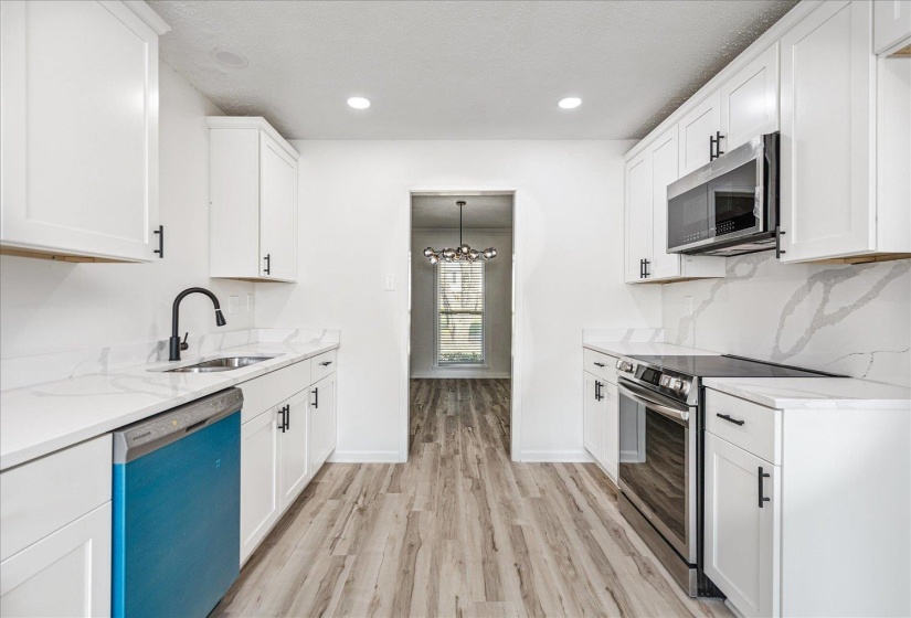 Modern kitchen featuring white shaker cabinetry, light-toned wood-finish flooring, and white countertops with a matching backsplash