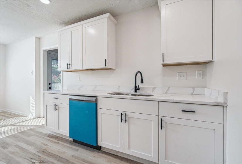Modern kitchen featuring white shaker cabinetry, stone-finish countertops, an undermount sink with a matte black faucet, and wood-finish flooring