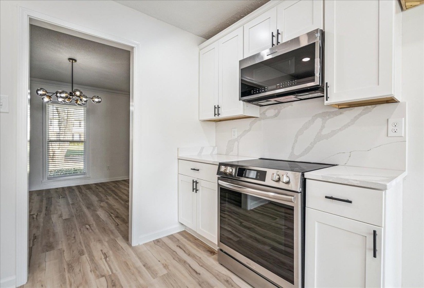 Modern kitchen featuring white cabinetry with black hardware, stainless steel appliances, a white patterned backsplash, and light wood-finish flooring