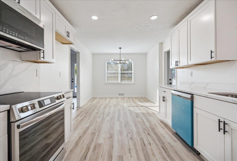 Modern kitchen featuring white cabinetry with matte black hardware, stainless steel appliances, white quartz countertops, and wood-finish flooring