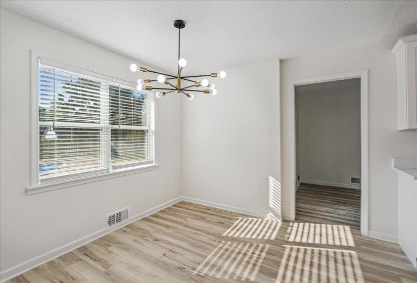 Spacious room featuring wood-finish flooring, a contemporary black and brass chandelier, and a large window with white blinds