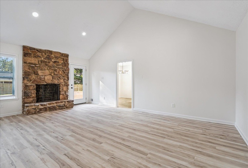 Spacious room featuring a stone fireplace, wood-finish flooring, and a vaulted ceiling
