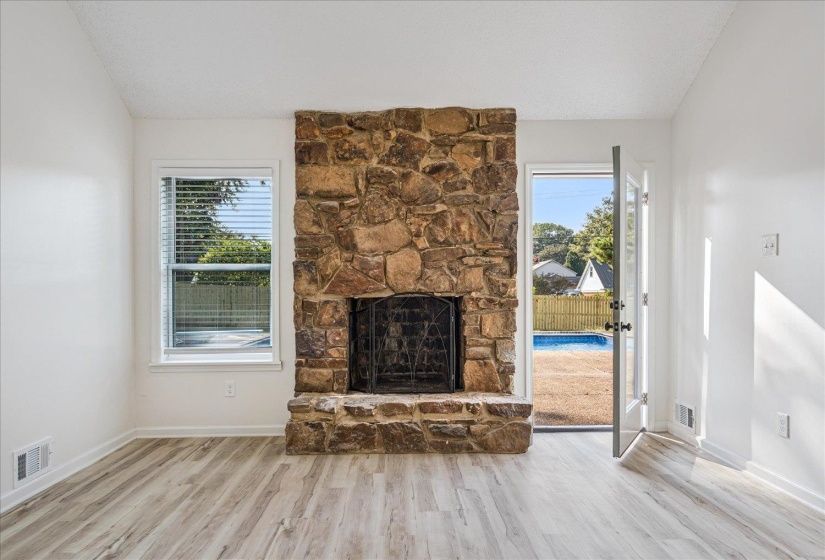 Stone fireplace with iron grate, wood-finish flooring, and white walls