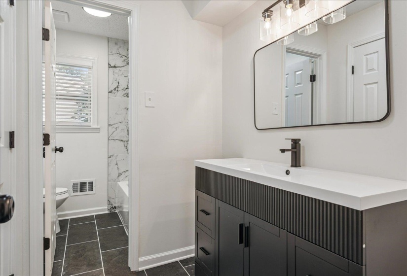 Bathroom vanity featuring a white countertop with an integrated sink, matte black faucet, and a black framed mirror