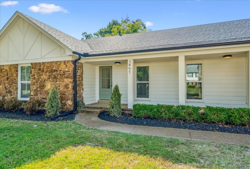 Stone and siding facade featuring a covered entry porch, dark grey architectural shingle roof, and a light green entry door