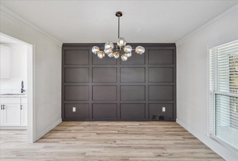 Dining area featuring a dark accent wall with panel molding, a multi-bulb chandelier, and wood-finish flooring
