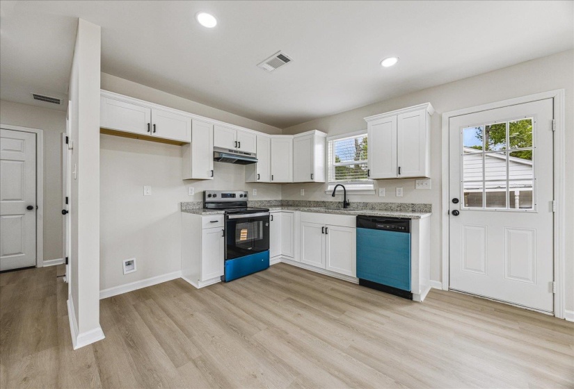 Modern kitchen with light wood-finish flooring, white cabinetry, and granite countertops