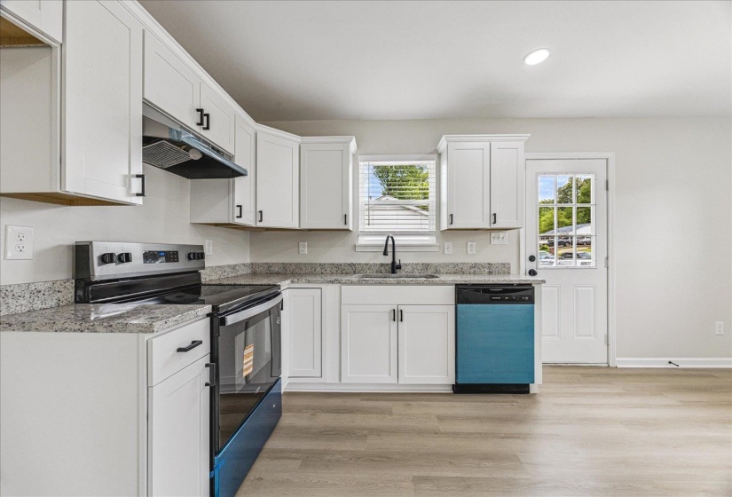 Modern kitchen featuring white cabinetry with black hardware, stone-finish countertops, stainless steel appliances, and wood-finish flooring