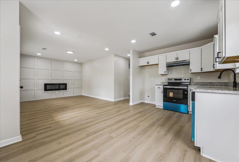 Open-concept living space with wood-finish flooring, recessed lighting, and a feature wall with an integrated fireplace