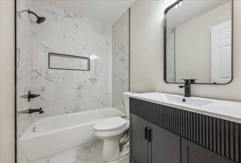 Bathroom featuring a white bathtub with a black shower fixture, a built-in shower niche, and white marble-look wall tiles