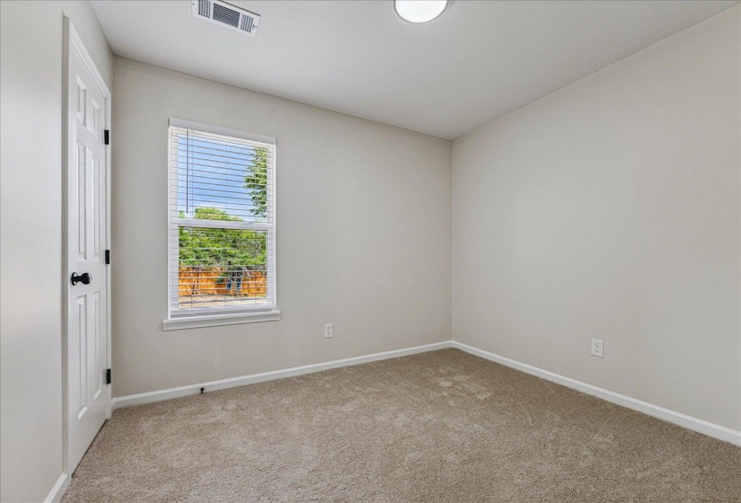 Neutral-toned room featuring a single window with horizontal blinds, light-colored carpet flooring, and a white paneled door with black hardware