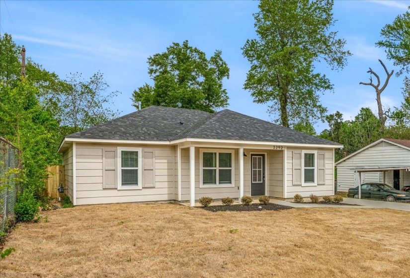 Single-story residence featuring light-toned horizontal siding, a covered front entry, dark composite shingle roofing, and decorative window shutters