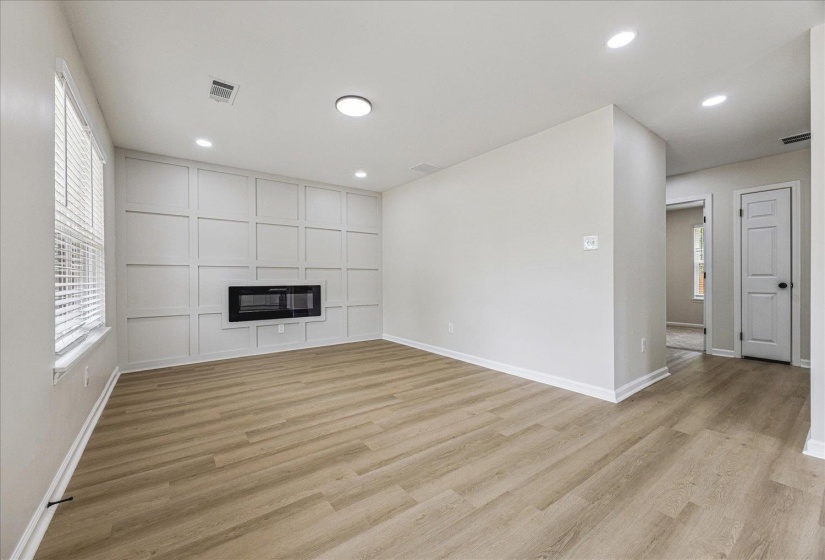 Spacious interior featuring wood-finish flooring, a decorative accent wall with an integrated fireplace, recessed lighting, and a large window with blinds