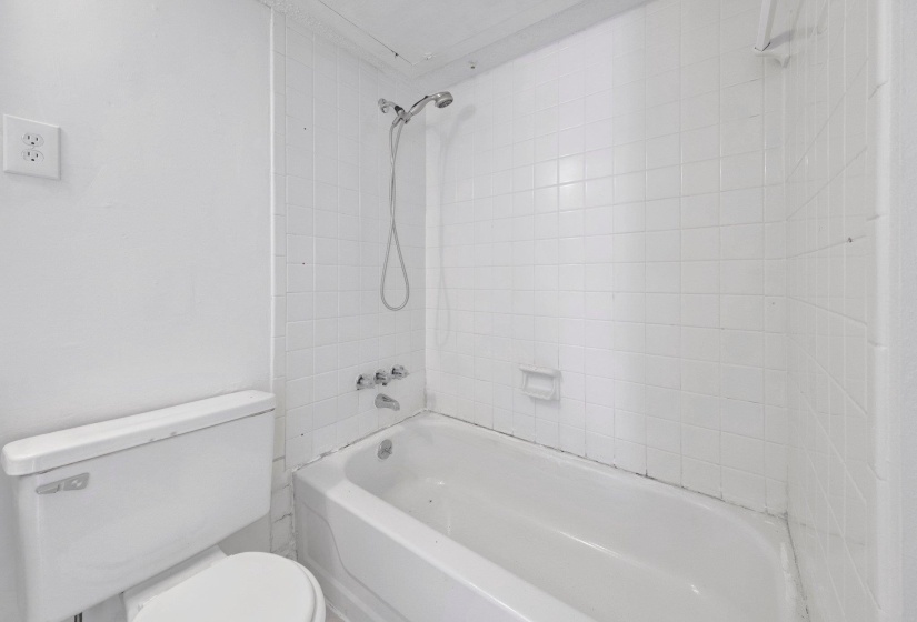 White tiled shower and tub combination with a fixed showerhead and wall-mounted faucet