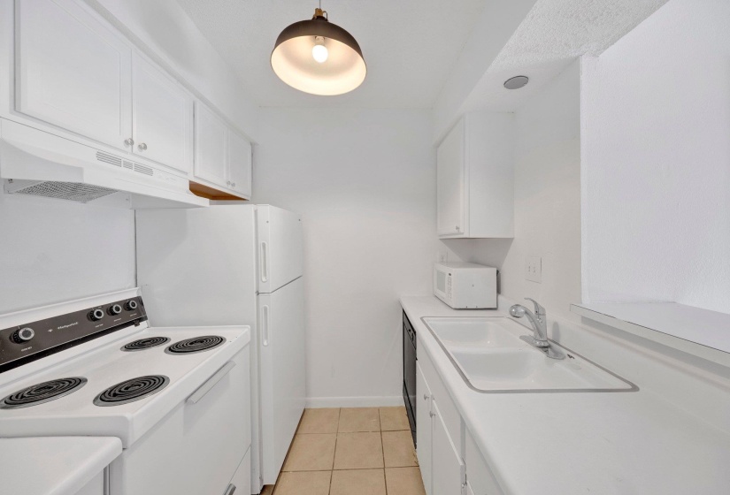 Galley kitchen featuring white cabinetry, a double basin sink, neutral tile flooring, and integrated appliances