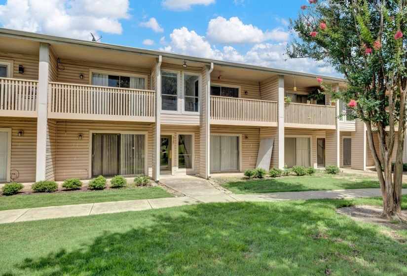 Two-story multi-unit dwelling with horizontal siding, individual balconies with slatted railings, and ground-level patios