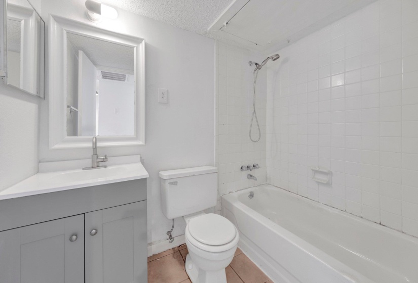Bathroom featuring a white subway tile tub surround, white bathtub, and a modern gray vanity with a single basin sink