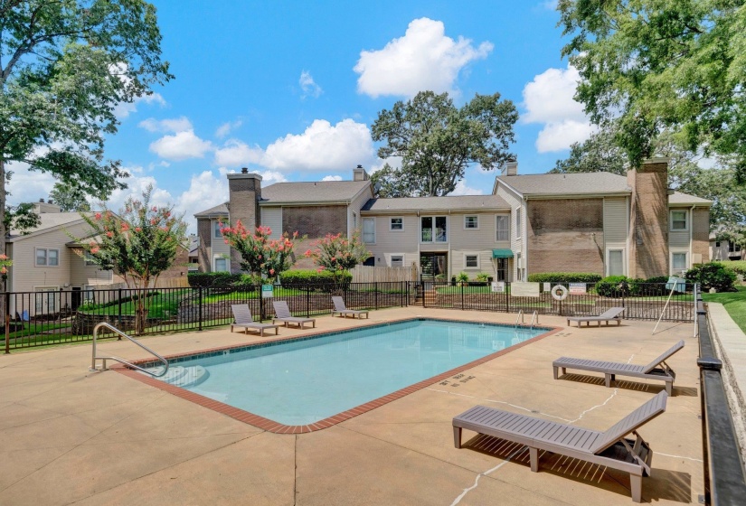 Community swimming pool with a concrete surround, surrounded by a black metal fence