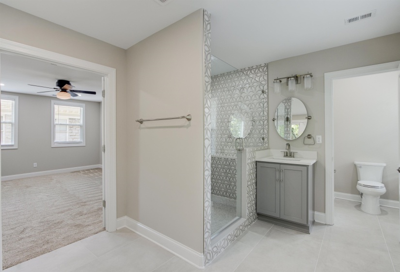 Bathroom featuring toilet, vanity, tiled shower, ceiling fan, and tile patterned flooring
