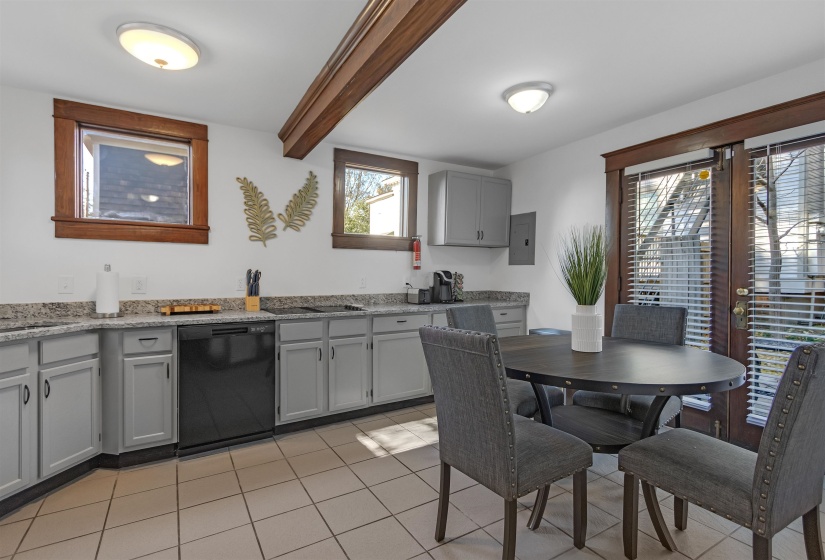 Kitchen featuring black dishwasher, beam ceiling, light tile patterned flooring, gray cabinets, and electric panel