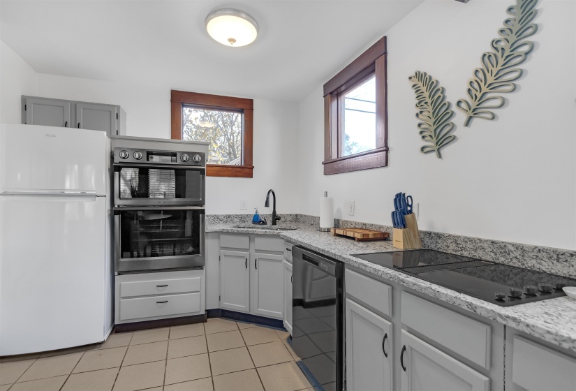 Kitchen with black appliances, a sink, light tile patterned floors, and light stone countertops