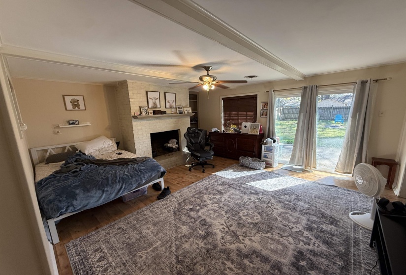 Bedroom featuring wood finished floors, beamed ceiling, a brick fireplace, ceiling fan, and ornamental molding
