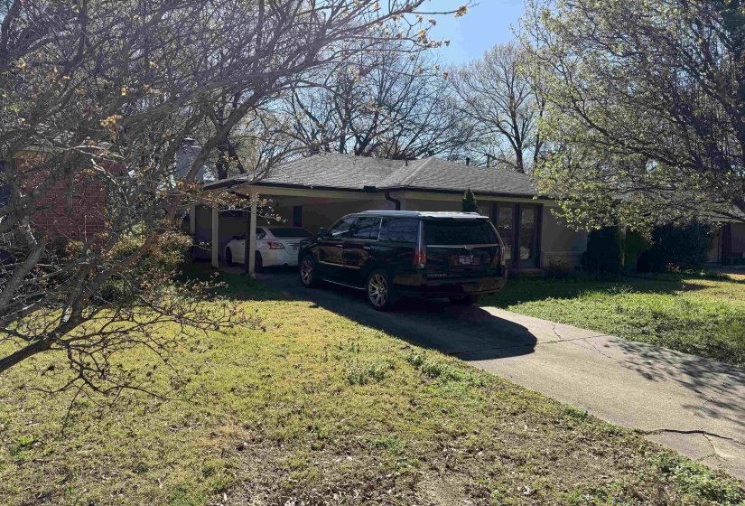 View of front of house with a front yard, roof with shingles, driveway, and an attached carport